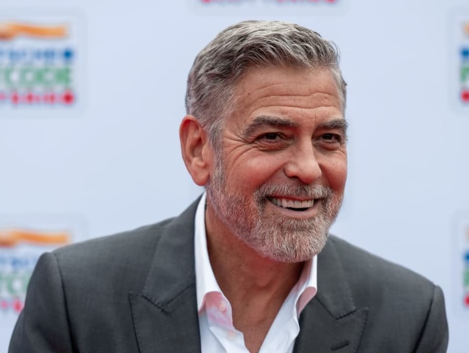 George Clooney lachend auf bei einem Anlass. 