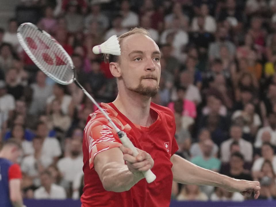 Badmintonspieler im roten Trikot schlägt mit Schläger auf den Federball.