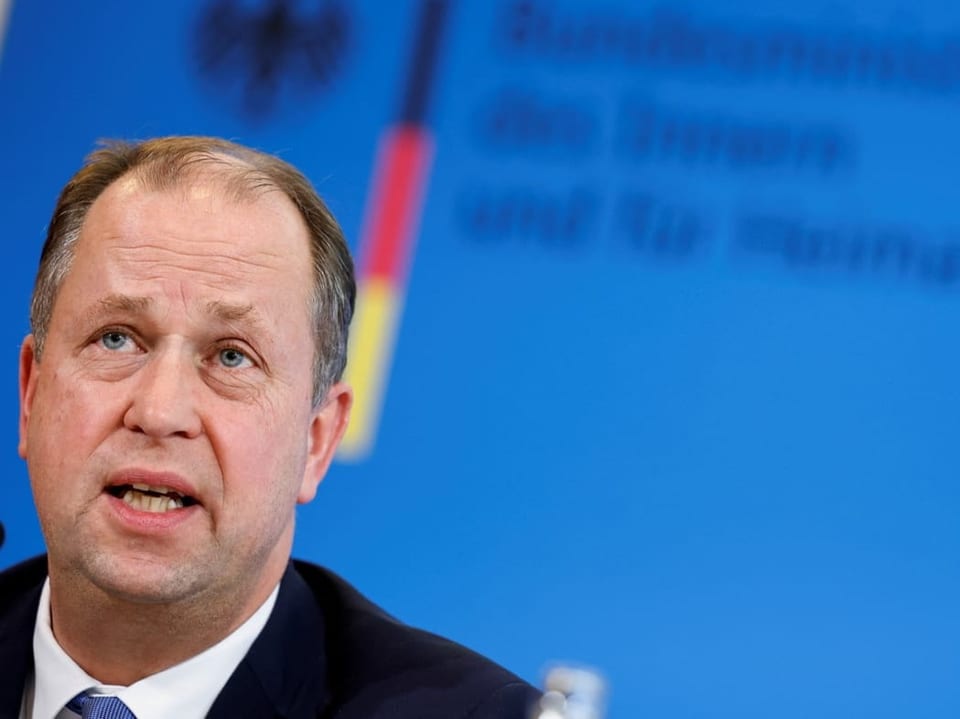 Mann spricht auf einer Pressekonferenz vor einer blauen Wand.