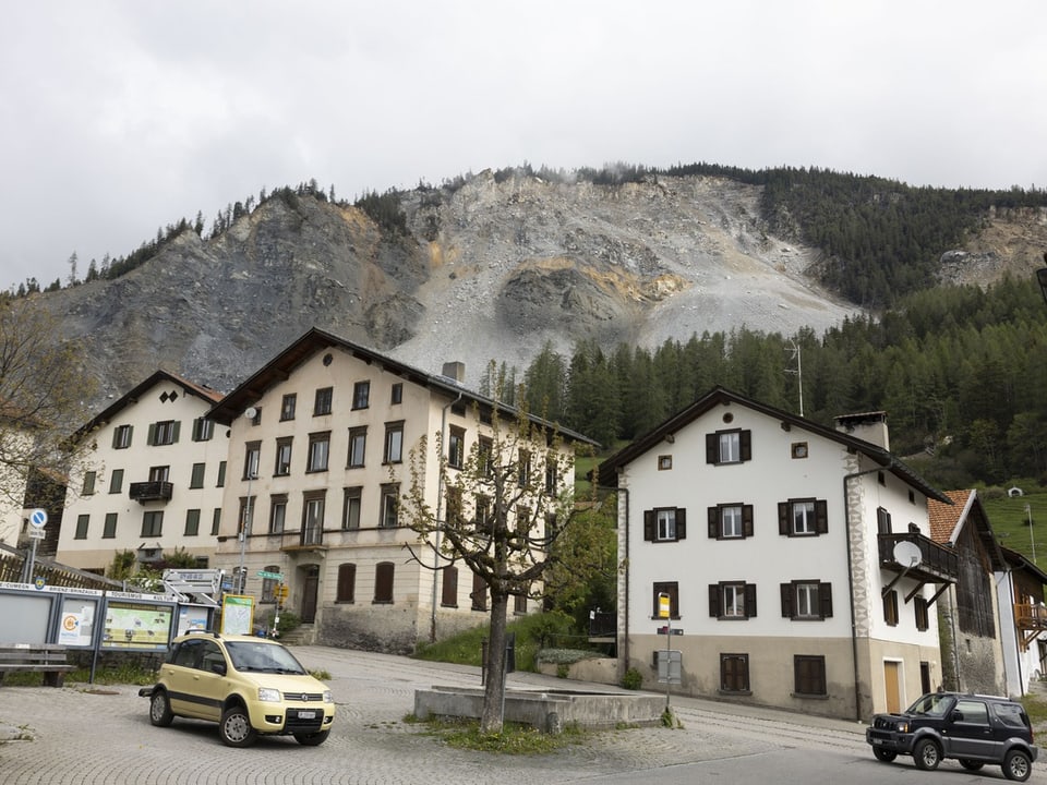 Dorf mit Berg im Hintergrund und Autos im Vordergrund.