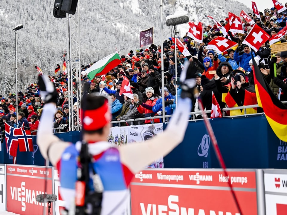 Skifahrer jubelt vor jubelnder Menge mit Fahnen.