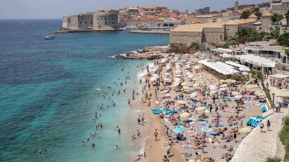 Blick von oben auf prall gefüllten Strand; im Hintergrund ist die Alstastadt von Dubrovnik zu sehen