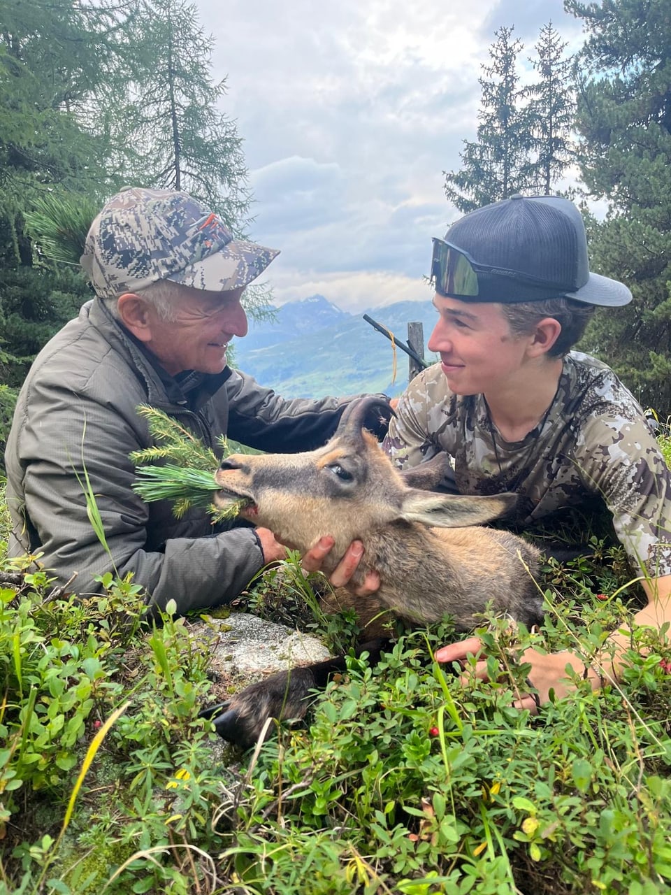 Zwei Menschen lächeln und halten ein Tier im Wald.