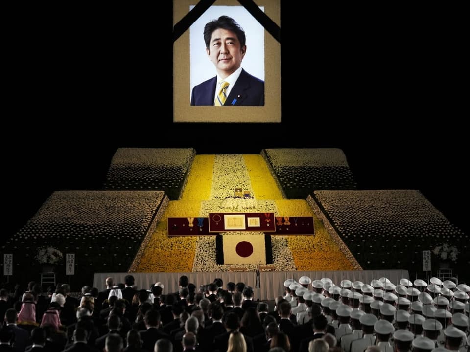 Viele Menschen stehen während der Beerdigung vor einem grossen Porträt von Shinzo Abe.