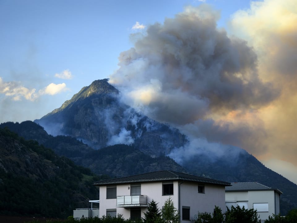 Haus vor brennendem Berg mit starkem Rauch.