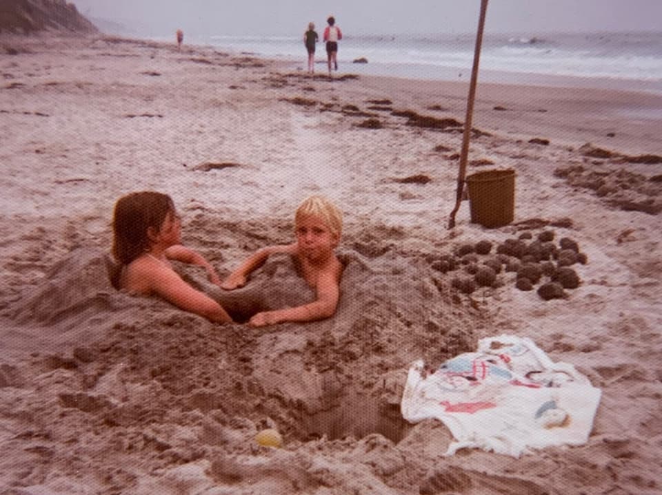 Zwei Kinder, die sich im Sand eingebuddelt haben.