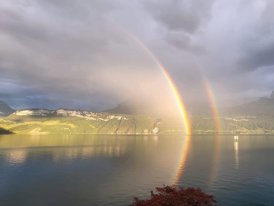 Doppelter Regenbogen über einem See mit Bergen im Hintergrund.