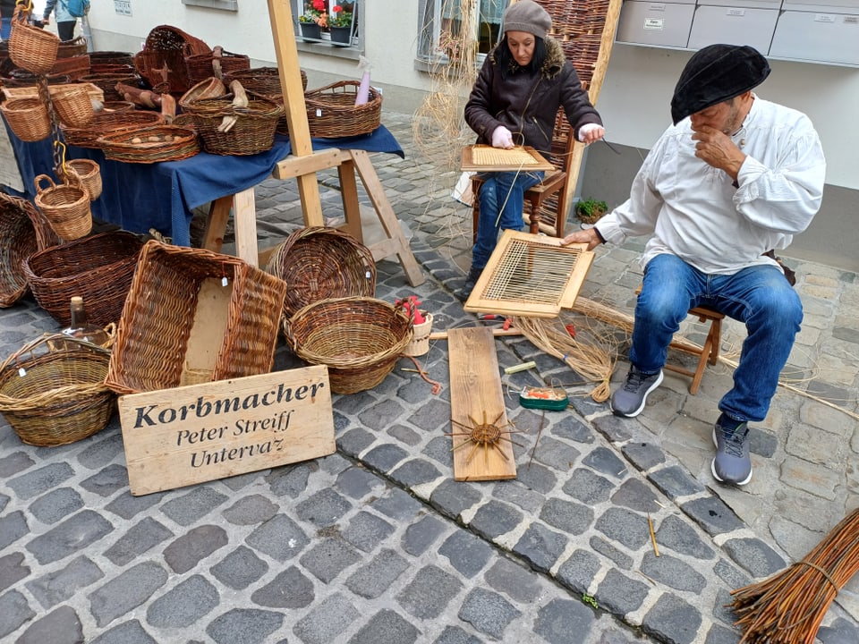 Korbmacher bei der Arbeit auf einem Markt, umgeben von Körben.