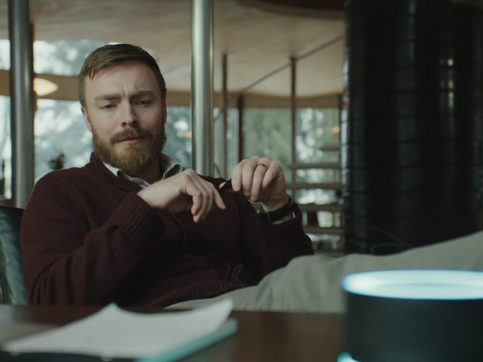 Man sitting at desk, looking at glowing device on table.