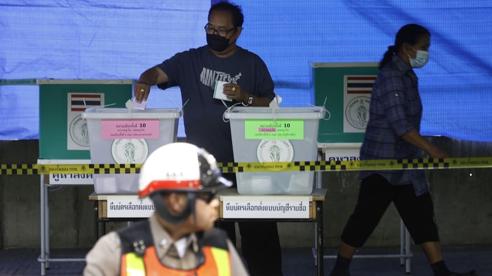 Ein Wähler wirft einen Abstimmungszettel in die Wahlurne, im Vordergrund ein Polizist