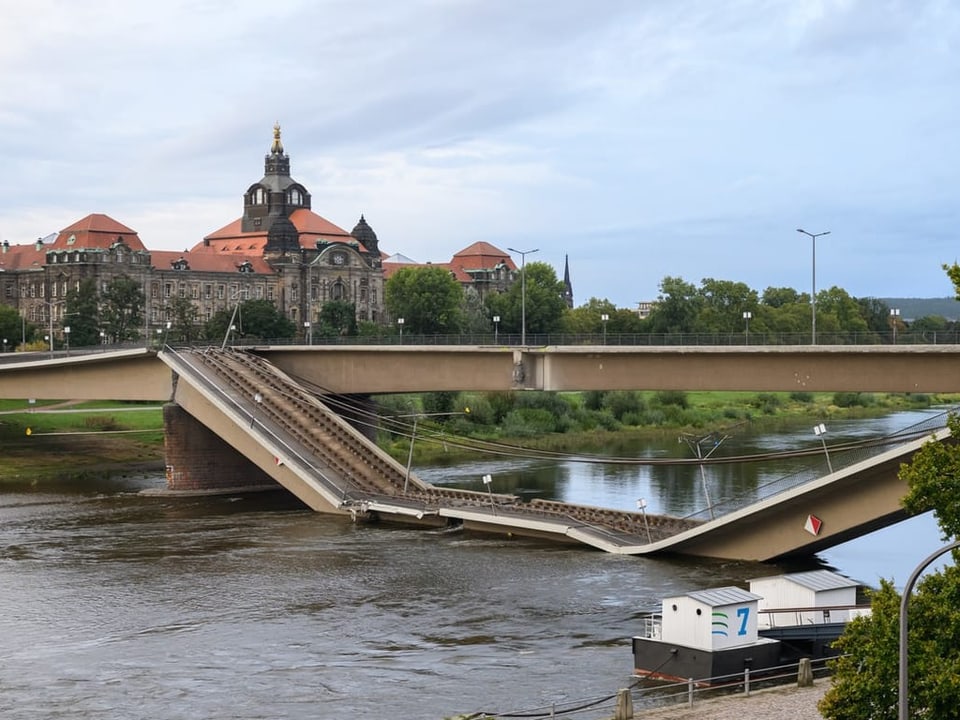 Eingestürzte Brücke über einem Fluss mit historischem Gebäude im Hintergrund.