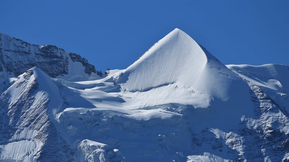 Schneebedeckter Berggipfel unter blauem Himmel.