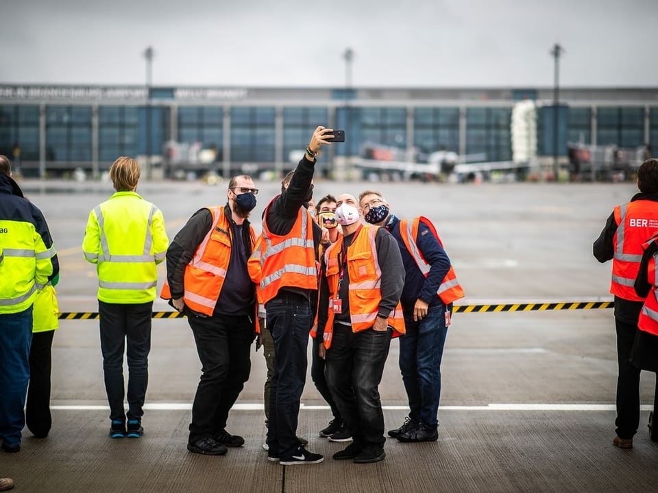 Mitarbeiter machen ein Selfie vor dem neuen Flughafen.