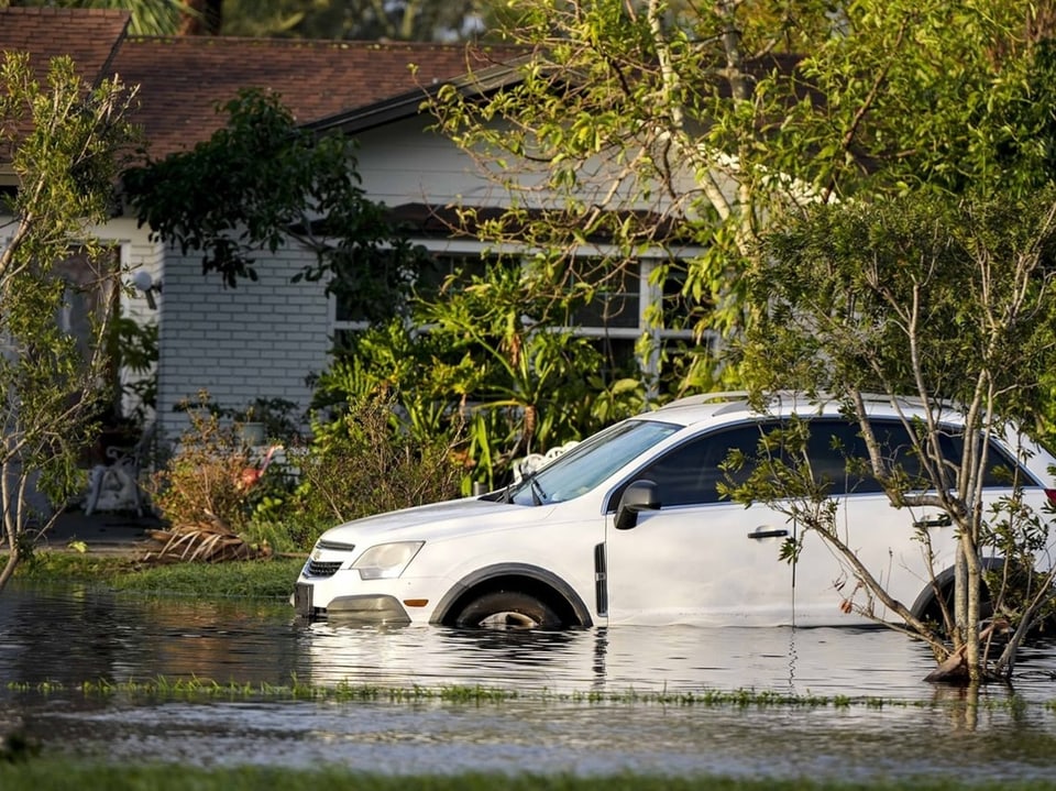 Weisses Auto im Hochwasser vor einem Haus.