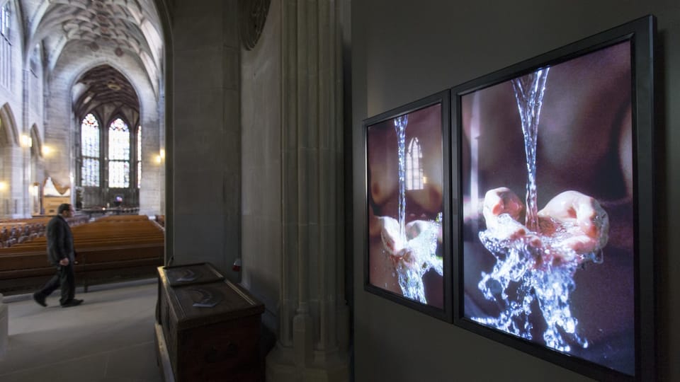 Kunstinstallation in Kirche mit zwei digitalen Bildschirmen neben Kirchenbänken.