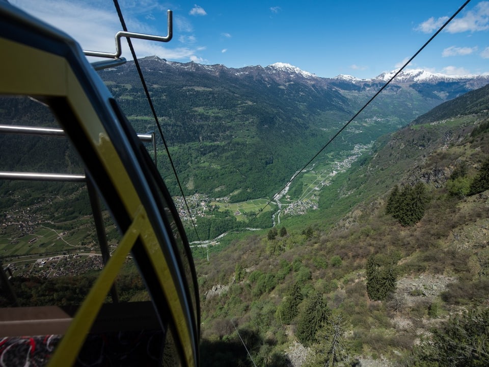 Blick aus Seilbahn auf grünes Tal und schneebedeckte Berge.