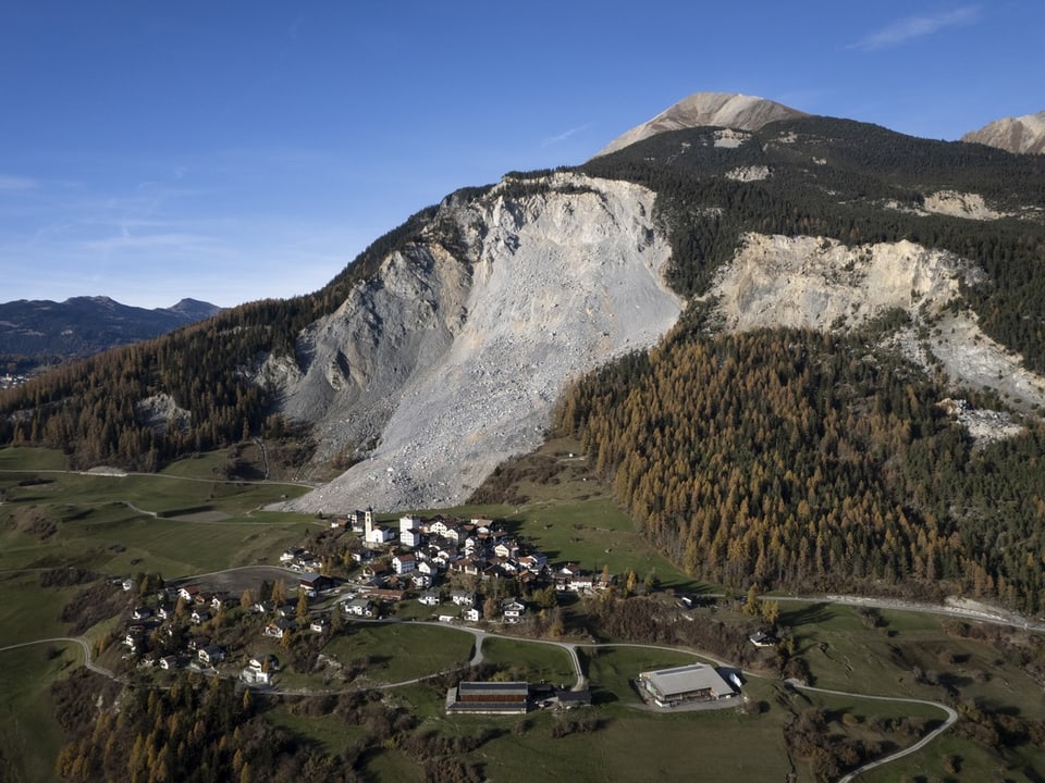 Luftaufnahme eines Dorfes vor einem grossen Berghang mit Geröll.