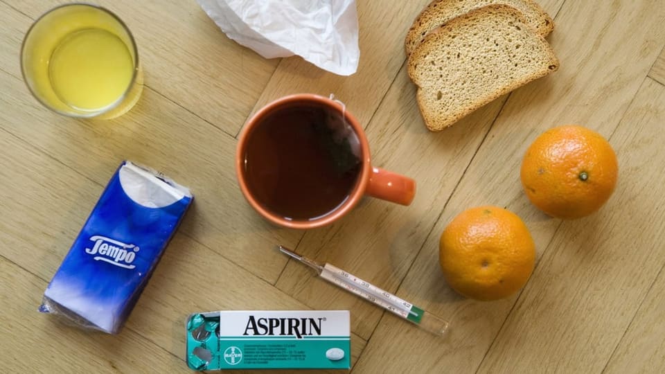 Dinge, die man bei einer Erkältung nutzt wie Tee, Taschentuch, Fiebermesser, Mandarine, Brot und Medikamente