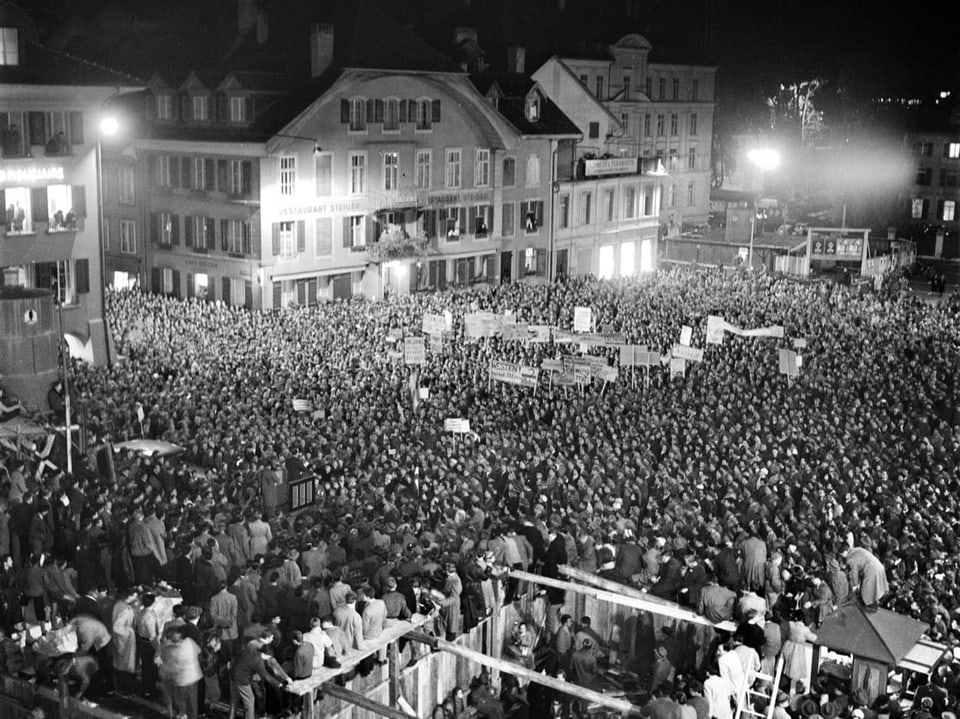 Grosse Menschenmenge versammelt auf einem Platz bei Nacht.