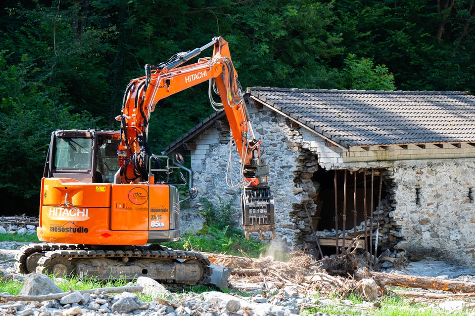 Bagger reisst altes Steingebäude ein.