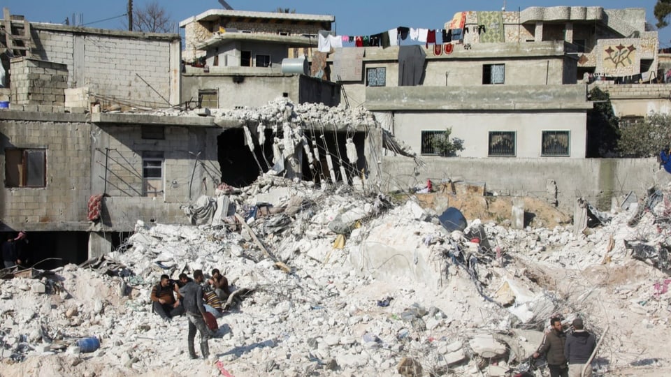 Menschen sitzen vor zerstörten Häusern in Harim im Nordwesten Syriens.