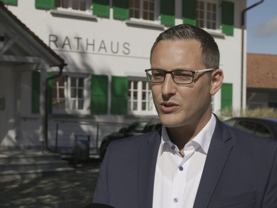 Mann mit Brille vor einem Rathaus stehend.