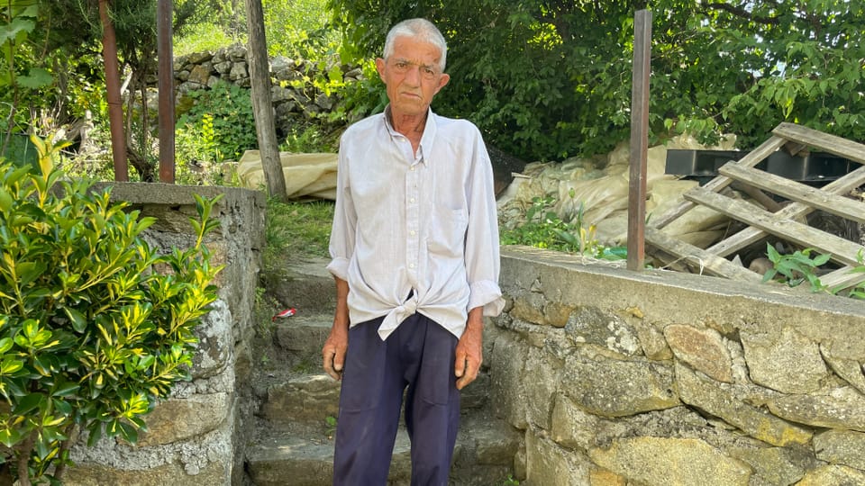 Älterer Mann steht vor einer Steinwand im Garten.