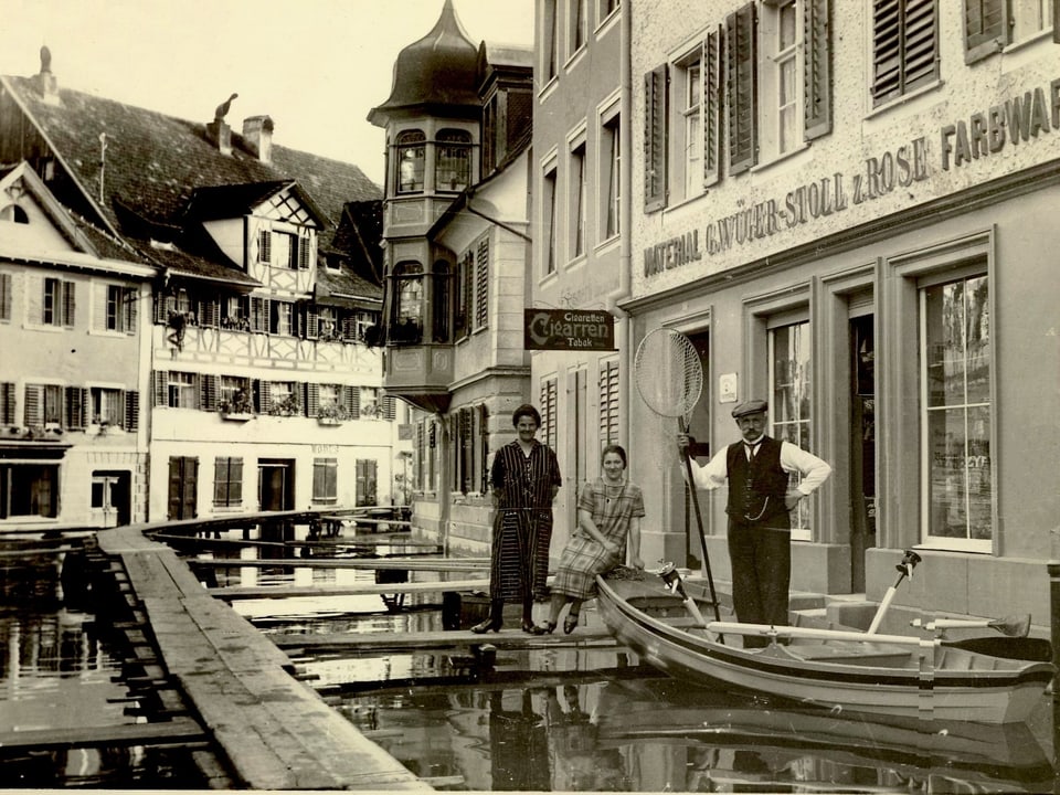 Personen mit Boot in überfluteter Stadtgasse, historische Aufnahme.