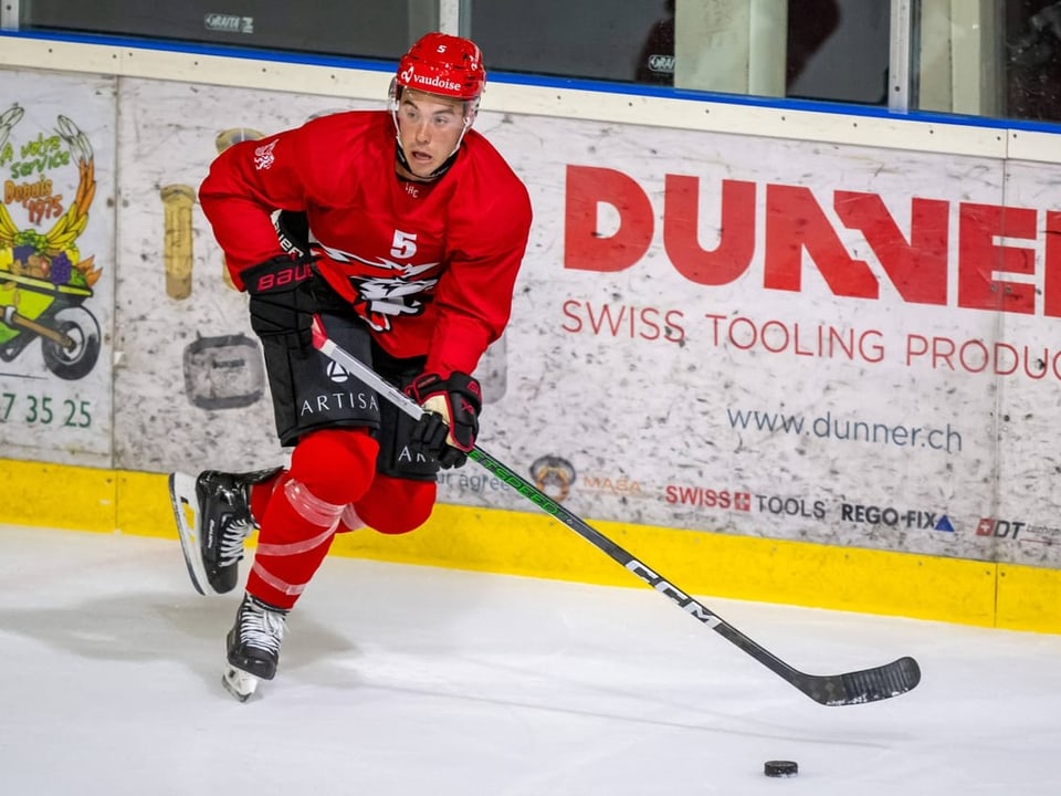 Eishockeyspieler in roter Uniform mit Puck auf dem Eis.