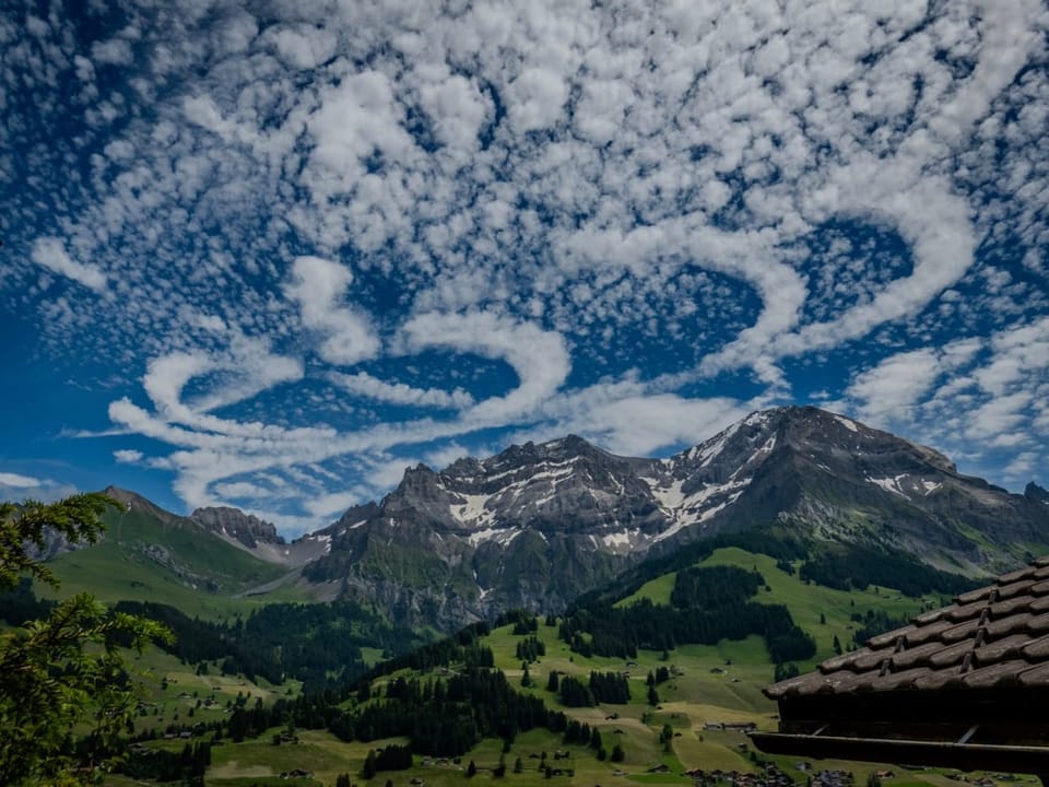 Blick auf ringförmige Wolken über Bergen und vor blauem Himmel.