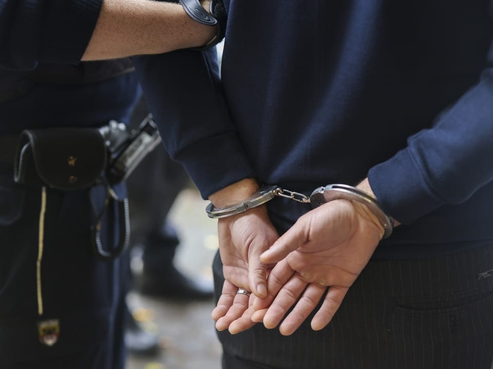 Person in Handschellen von Polizist festgehalten.