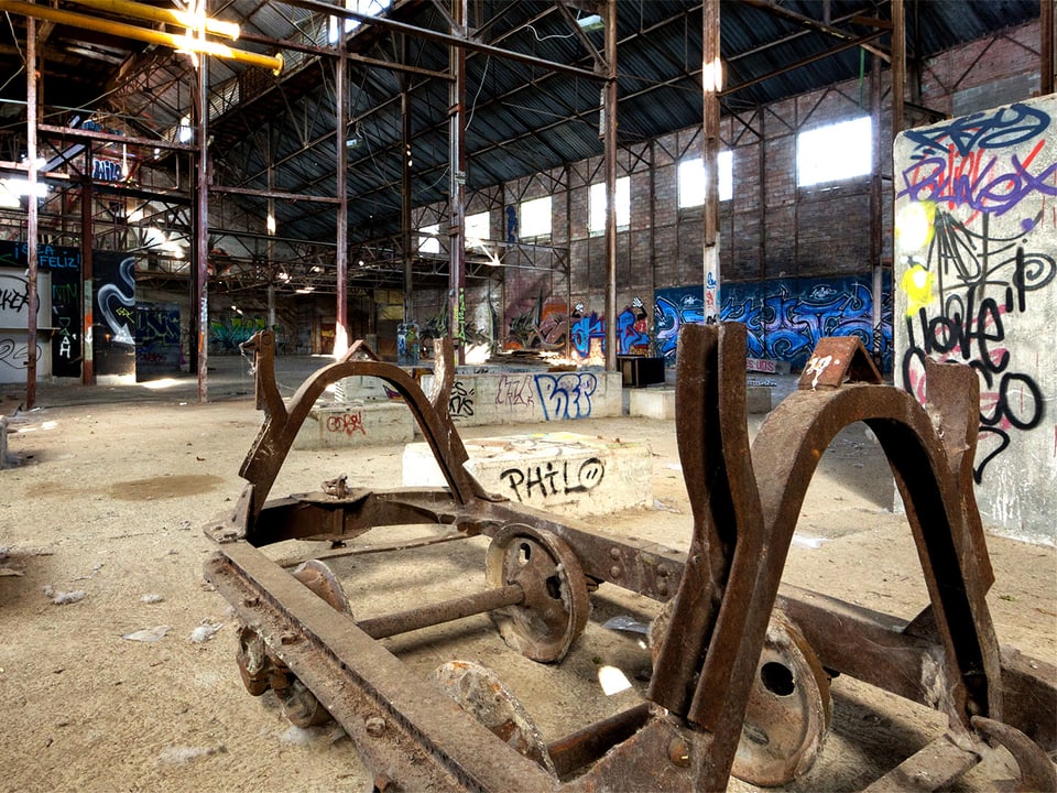 Ein roster Wagen mit Räder steht in einer leeren Fabrikhalle.