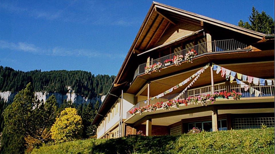 Berghaus mit blumengeschmücktem Balkon und Gebirgskulisse.