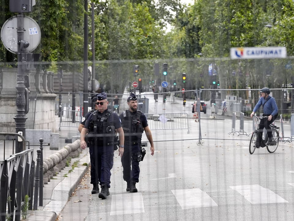 Zwei Polizisten gehen auf einer leeren Stadtstrasse, ein Mann fährt Fahrrad.