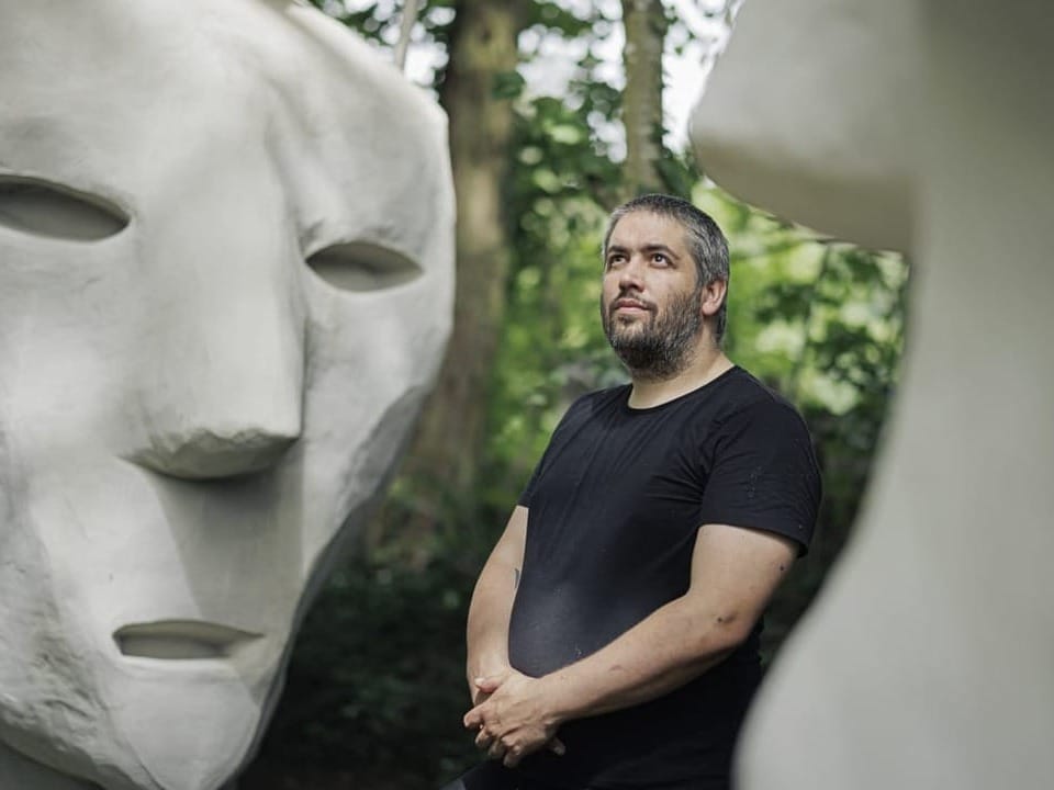 Augustin Rebetez steht im Garten zwischen seinen übergrossen Skulpturen in seinem Museum «Maison Totale».