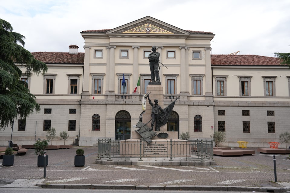 Standbild vor historischem Gebäude mit italienischer Flagge.