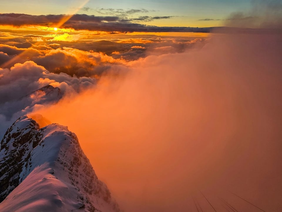 Sonnenuntergang über verschneitem Berggipfel und Wolken.