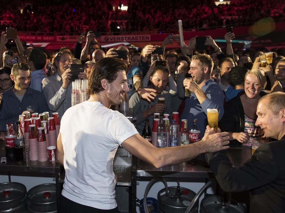 Fabian Cancellara schenkt Bier aus inmitten einer Menschenmenge.