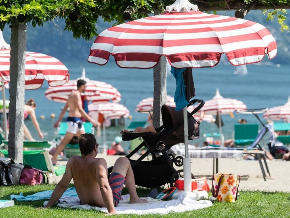 Menschen entspannen am Strand unter rot-weissen Sonnenschirmen.
