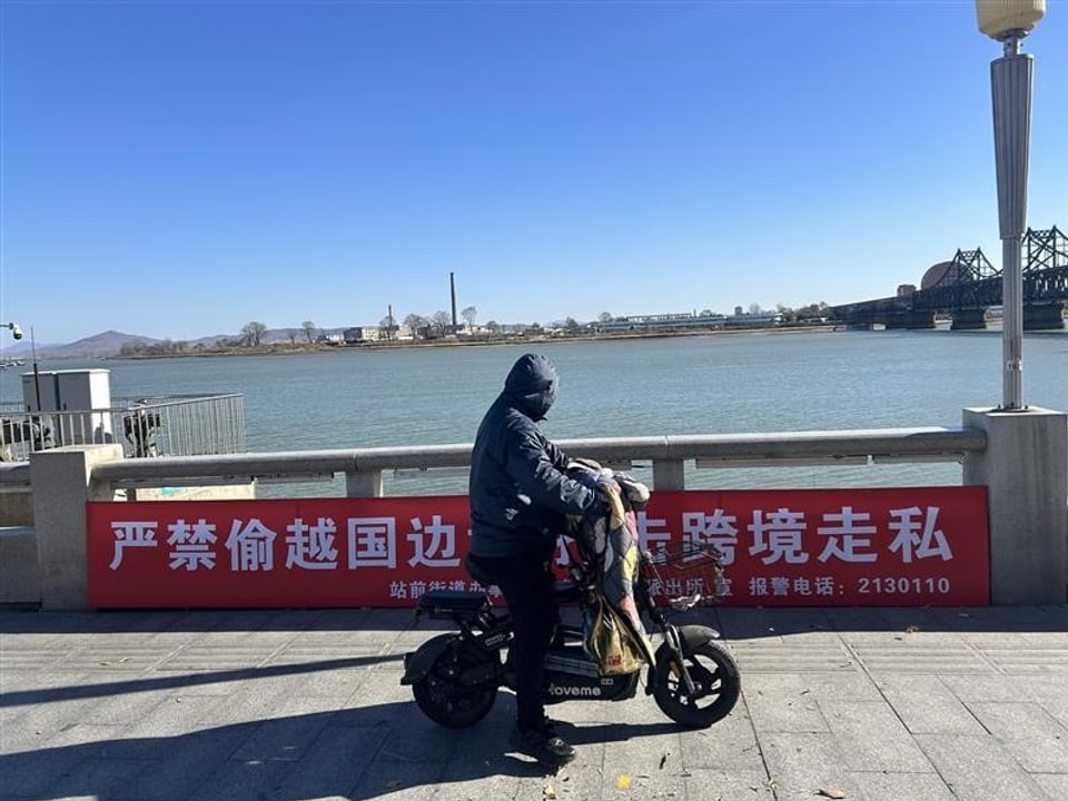 Person auf Fahrrad vor Fluss mit Warnschild.