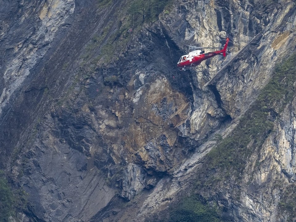 Roter Hubschrauber fliegt nah an einer Felswand vorbei.