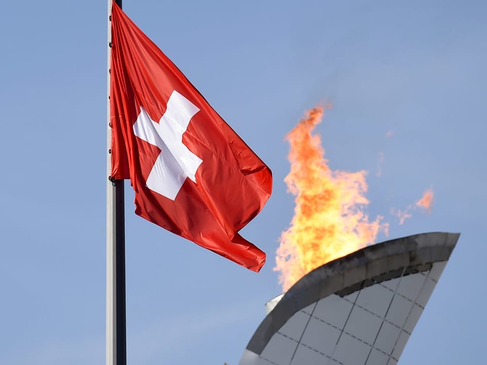 Schweizer Flagge neben olympischem Feuer.
