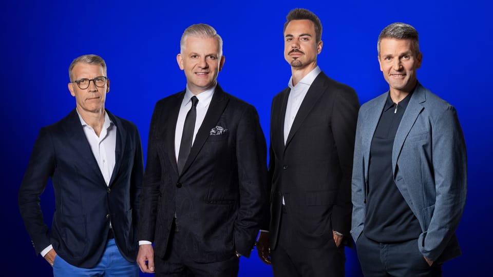 Vier Männer in formeller Kleidung vor blauem Hintergrund.