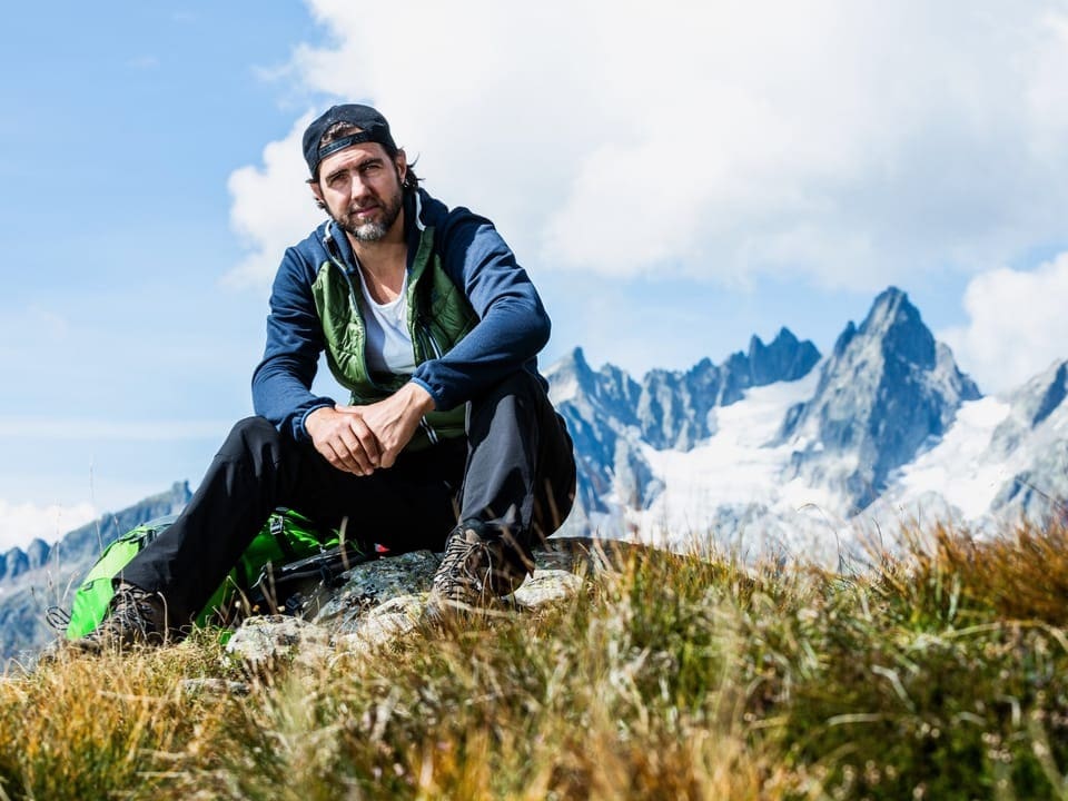 Mann sitzt in einer Bergwelt in Gras.