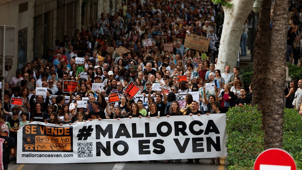 Menschenmenge bei einem Protest mit einem Banner, auf dem '#MALLORCA NO ES VEN' steht.