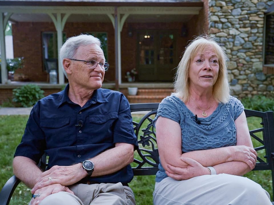 Ein älteres Ehepaar, Jay und Valerie Winzenried, sitzen vor ihrem Haus auf einer Bank.