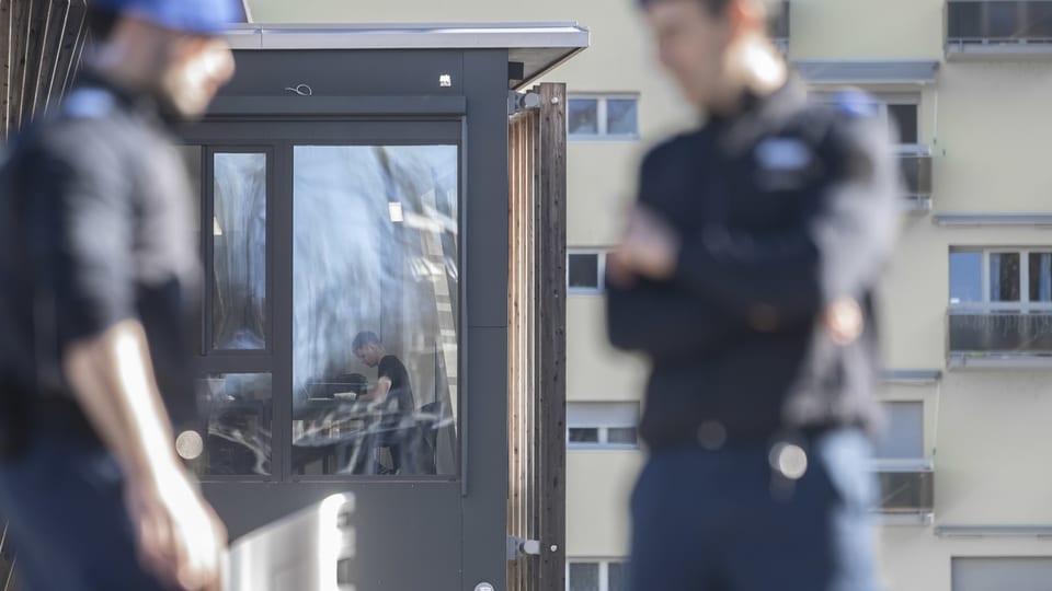 Zwei unscharfe Personen im Vordergrund, Mann in Kontrollraum im Hintergrund.