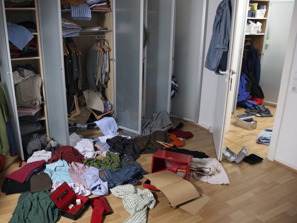 Ein Zimmer mit Schrank, Kleider und Gegenstände liegen am Boden verstreut.