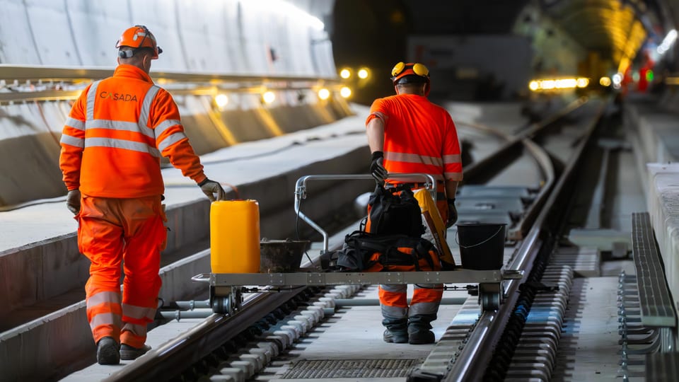 Zwei Arbeiter in orangener Kleidung bei der Arbeit in einem Eisenbahntunnel.
