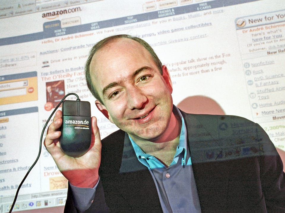 Mann hält eine Computermaus vor einem Bildschirm mit Amazon-Webseite.